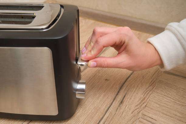 Hand pressing lever on a black stainless steel toaster on a wooden countertop.