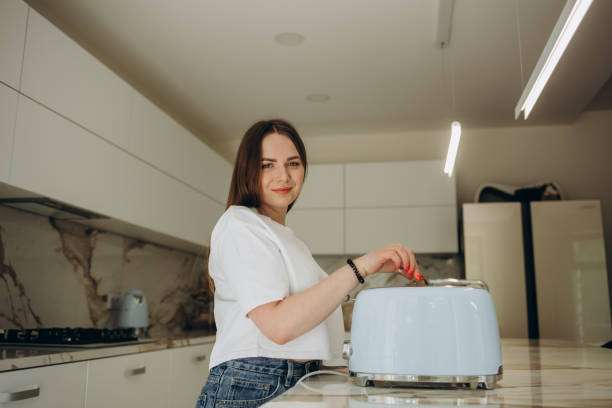 Young woman using toaster at table in kitchen.