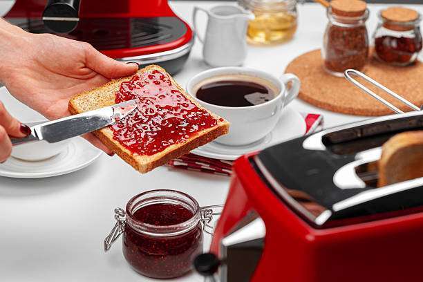 Female hand spresding strawberry jam on baked Toaster