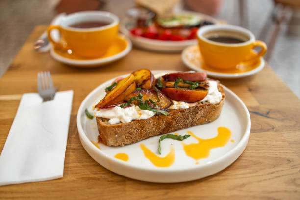 Toast with cream cheese, fresh juicy peach, almond and honey on a wooden tray.Toaster