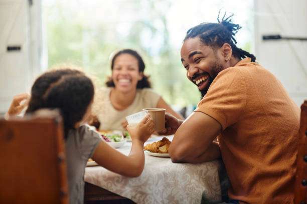 Happy African American father and daughter toasting with drinks while having a meal in dining room. Toaster