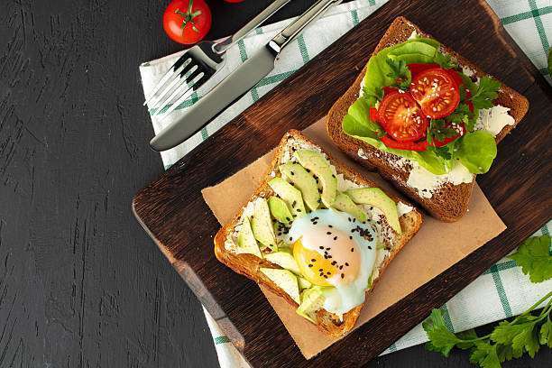 Fried toasts with avocado and egg, and with cream cheese and tomatoes on wooden board.Toaster