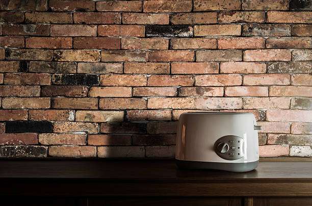 Modern two-slice toaster sitting on a wooden surface against a rustic brick wall.