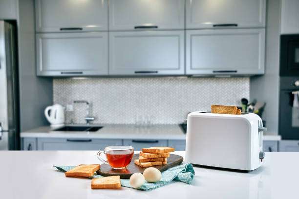 White toaster, stack of toast, tea, and eggs on a modern kitchen counter.