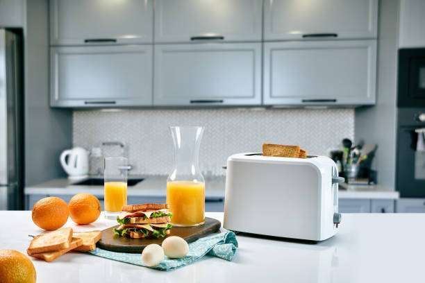 Modern kitchen counter with a white toaster, orange juice, and a breakfast sandwich.