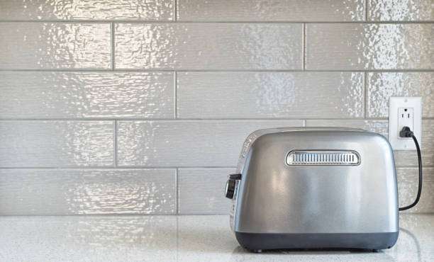 Sleek silver toaster plugged into an outlet on a clean white tiled kitchen counter.