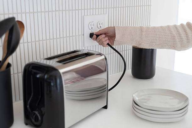 Hand plugging a sleek silver toaster into a kitchen outlet.