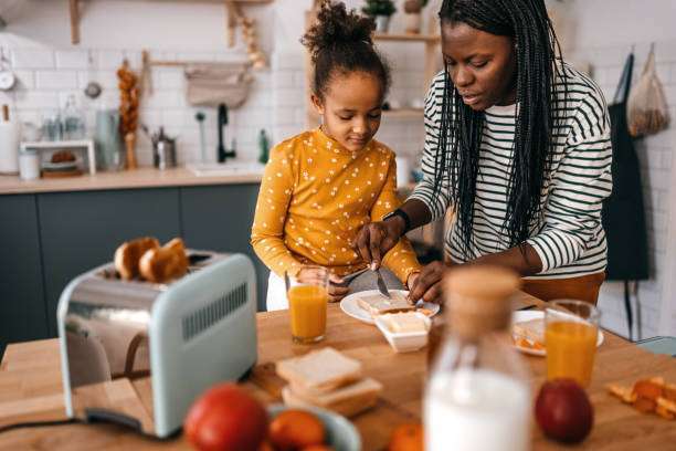 Mother and child preparing breakfast with a light blue toaster on a wooden table.