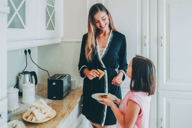 Mother and daughter making toast with a black toaster in a bright kitchen.
