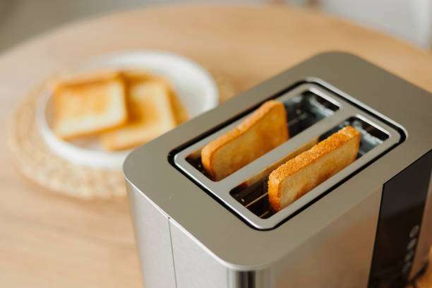 Freshly toasted bread slices pop out of a modern stainless steel toaster on a table.