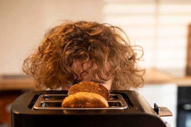 Curious child peeking over a black toaster as golden brown toast pops up.