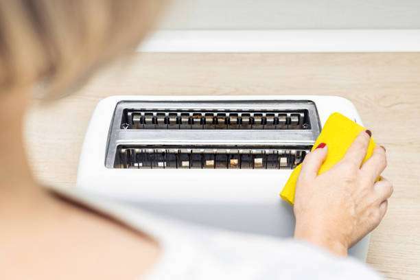 Person's hand cleaning the inside of a white toaster with a yellow sponge.