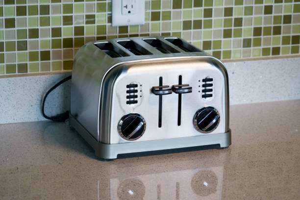 Shiny stainless steel 4-slice toaster sitting on a kitchen counter with a tiled backsplash.